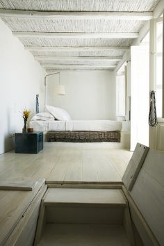 a room with white walls and wooden floors, stairs leading up to the bed area