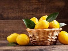 a wicker basket filled with lemons on top of a wooden table next to leaves