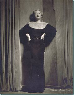 an old black and white photo of a woman standing in front of curtains with her hands on her hips