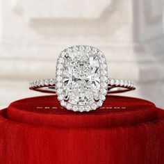 a cushion cut diamond ring on top of a red velvet box