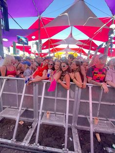 a group of people sitting under umbrellas at an outdoor music festival in the sun