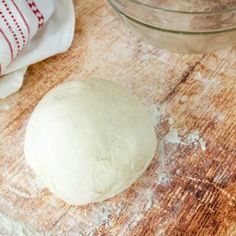 a ball of dough sitting on top of a wooden table next to a glass bowl