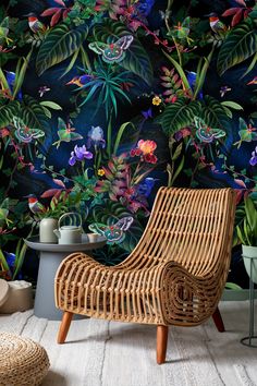 a wicker chair sitting in front of a wall with flowers and plants on it