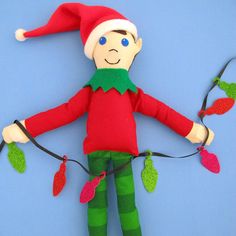 an elf doll with christmas lights hanging from it's arms on a blue background