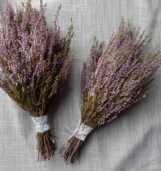 two bundles of dried lavender flowers sitting on top of a gray cloth covered tablecloth