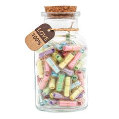 a glass jar filled with lots of colorful beads and wooden spools on a white background