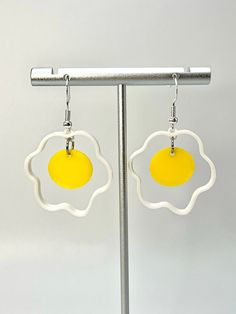 pair of yellow and white earrings with an egg in the center on a metal stand