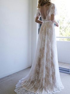 a woman in a wedding dress standing by a window looking out the window with her back to the camera