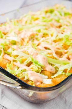 a casserole dish with lettuce, cheese and dressing in it on a table