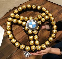 a person holding up a gold belt made out of chocolate balls and bmw emblems