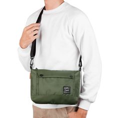 a man wearing a white sweater and khaki pants holding a green messenger bag