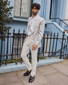 a man in a white suit and tie standing on the sidewalk next to a blue building