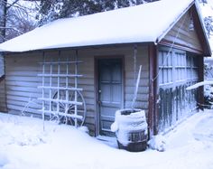 an old log cabin covered in snow with a wheel leaning against the door and window