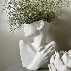 a white vase with flowers in it sitting on a table next to a planter