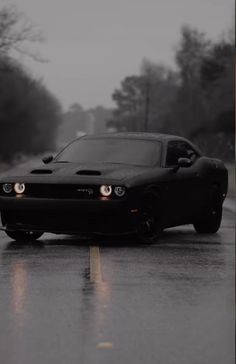 a black sports car driving down the road in the rain with headlights on it's headlamps