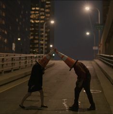 two people with traffic cones on their heads are walking down the street at night time