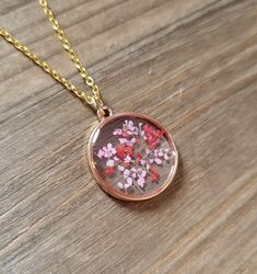 a necklace with pink and red flowers in it on a wooden surface, hanging from a gold chain