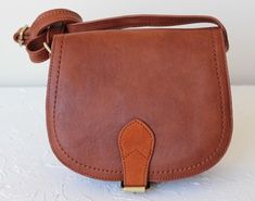 Cognac brown saddle bag. Supple textured faux leather looks like the real thing (5% leather, 95% polyurethane). 100% polyester brown faux suede lining. Adjustable cross body and/or shoulder strap (53" long when fully extended). Magnetic front closure. Interior pocket underneath flap. Measures approx. 8" wide x 7" high x 2 1/2" deep. Brown Saddle Bag, Crossbody Saddle Bag, Saddle Bag, Saddle Bags, Cognac, Faux Suede, Saddle, Cross Body, Fashion Bags