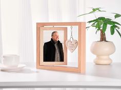 a wooden frame with a photo and a heart hanging from it on a table next to a coffee cup