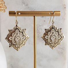 a pair of gold - tone earrings with intricate filigrees are displayed on a stand