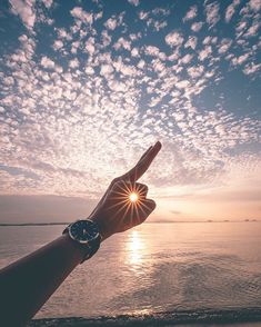 a person's hand pointing at the sun with clouds in the sky above them