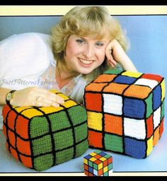 a woman laying on the floor next to two rubik cubes, one made out of crochet