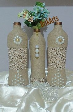 three vases with beads and pearls on them sitting on a white satin table cloth