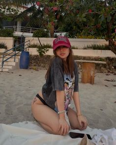 a young woman sitting on the beach wearing a hat