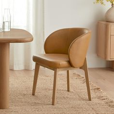 a brown leather chair sitting in front of a wooden table with a vase on it