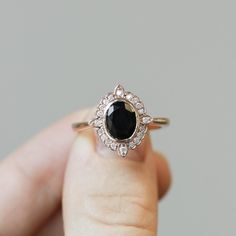 a woman's hand holding a ring with a black stone and diamond accents on it