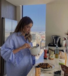 a woman standing in front of a kitchen counter holding a bowl with food on it