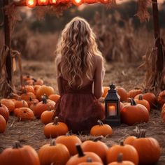 a woman sitting on the ground in front of pumpkins with candles lit up behind her