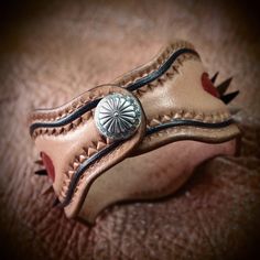 This leather wristband uses a single layer of plush natural vegetable tanned leather which is designed, carved, stamped and dyed with a Native Old West theme. A bold concho sits in the center and a smaller fluted concho serves as a snap closure. kangaroo lace details add to the Southwestern Style Brown Concho Bracelets, Leather Concho Cuff Bracelet, Leather Cuff Bracelet With Concho, Western Style Brown Cuff Bracelet As Gift, Southwestern Hand Tooled Brown Cuff Bracelet, Western Hand Tooled Cuff Bracelet As Gift, Southwestern Hand-tooled Brown Bracelets, Western Style Leather Bracelet With Concho, Western Style Leather Bracelet With Concho As Gift