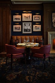 two red chairs sitting at a table in front of pictures on the wall above them