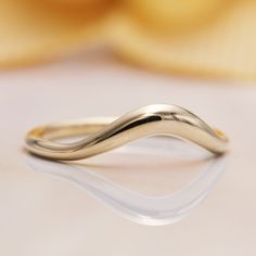 a close up view of a gold wedding ring on a white surface with a flower in the background