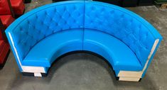 a blue curved couch sitting on top of a floor next to red and black chairs