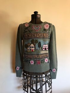 a green sweater with pink flowers on it sitting on top of a mannequin