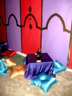 there is a small table with pillows on it in the middle of two walls that are painted purple, red and blue