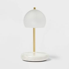 a white table lamp with a gold base on a white surface in front of a plain background