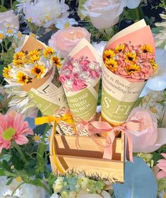 three flower boxes with flowers in them sitting on top of a wooden box surrounded by pink and yellow flowers