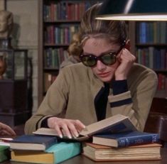 a woman sitting at a table with books and reading glasses on her head looking down