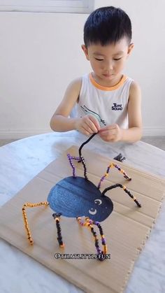 a young boy sitting at a table making a spider out of beads and wood sticks