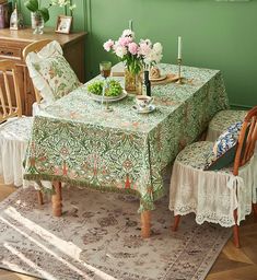 a dining room with green walls and floral table cloths on the table, two chairs