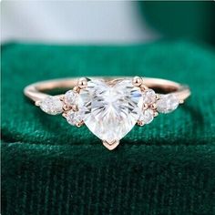 a heart shaped diamond ring sitting on top of a green cloth