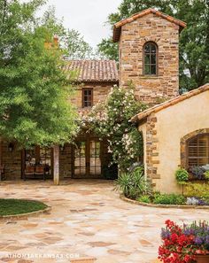 a stone house with trees and flowers in the front yard