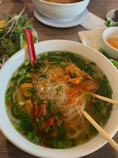 a bowl of soup with chopsticks in it on a table next to other bowls