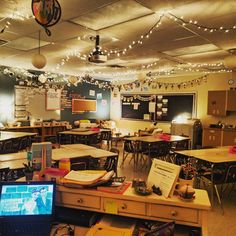 an empty classroom with desks and laptop on the floor, lights strung from the ceiling