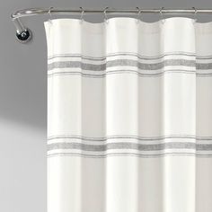 a white shower curtain with grey and white stripes on the bottom, in front of a gray wall