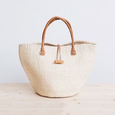 Rural Kamba women in Kenya hand-weave these beautiful handbags from tough sisal fibers. Sisal grows well in the semi-arid climate of eastern Kenya, and its spiky leaves contain long fibers that can be extracted for weaving.  approximate size: 10" diameter x 10" tall (without handle), 17" tall (with handle) leather hand Handwoven Rectangular Straw Bag In Neutral Color, Rectangular Handwoven Neutral Straw Bag, Eco-friendly White Bag With Natural Fiber, Eco-friendly White Bag In Natural Fiber, Cream Jute Straw Bag Handwoven, Cream Handwoven Jute Straw Bag, Handwoven Cream Jute Straw Bag, Natural Woven Jute Beach Bag, Natural Fiber Crochet Bag With Leather Handles