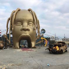 a large sculpture of a head with long hair on the ground next to an old car